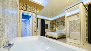 Une salle de bain moderne dotée d’une grande baignoire, d’un espace douche et d’une chambre séparée avec un lit et une coiffeuse.