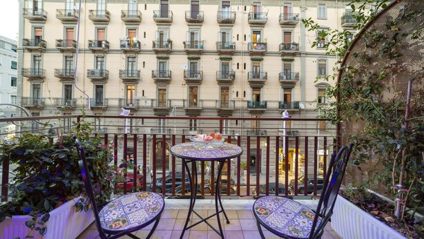 Un balcon avec deux chaises et une petite table, donnant sur un immeuble doté de nombreux balcons.