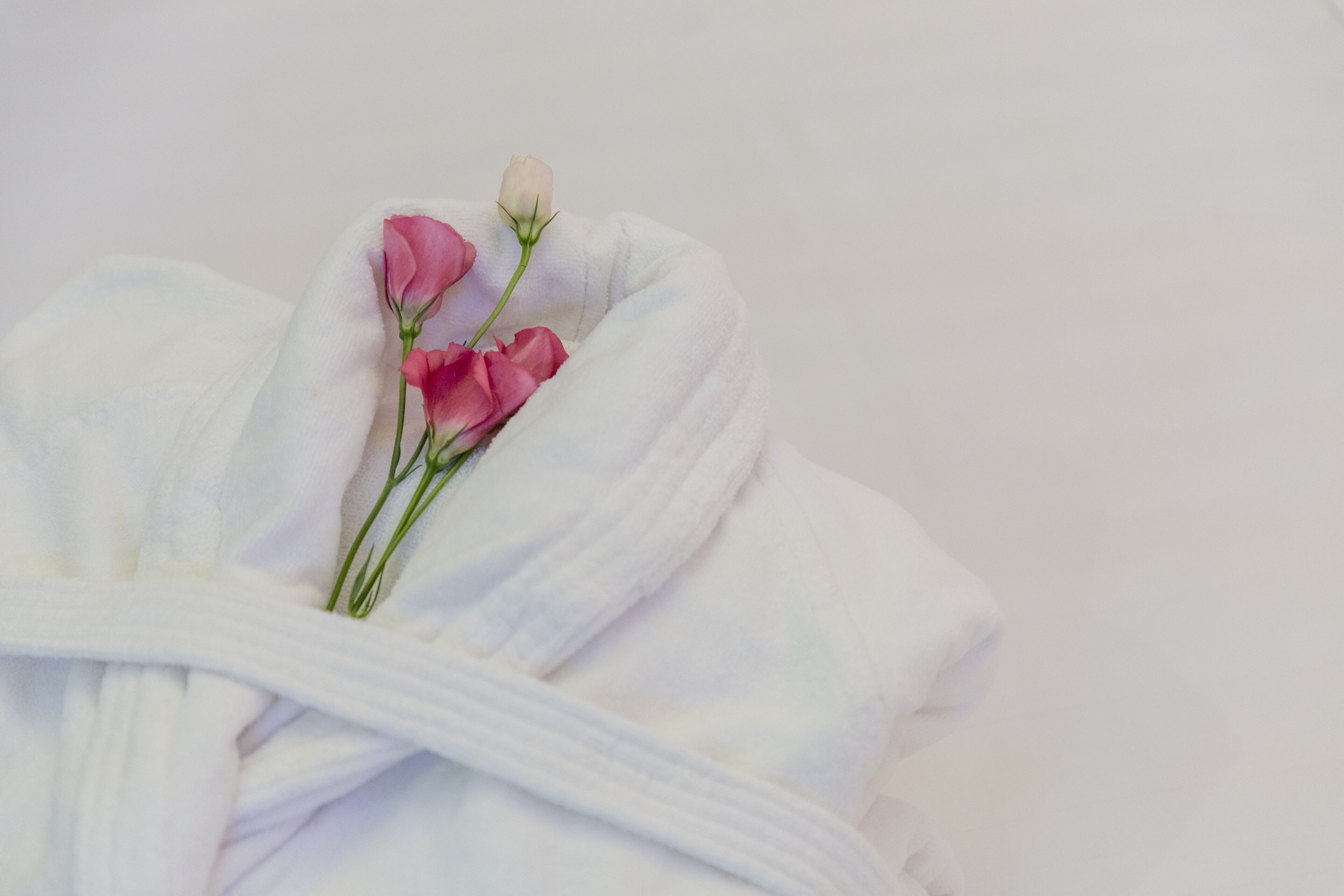 Ein ordentlich gefaltetes weißes Handtuch mit einer rosa Rose und einer weißen Rosenknospe.