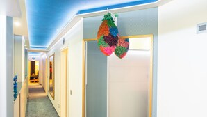 Un couloir d’hôtel avec un plafond bleu, une moquette à motifs et une porte ornée d’un élément décoratif suspendu.