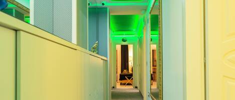 A narrow hallway with patterned carpet, green ceiling lights, and a door on the right.