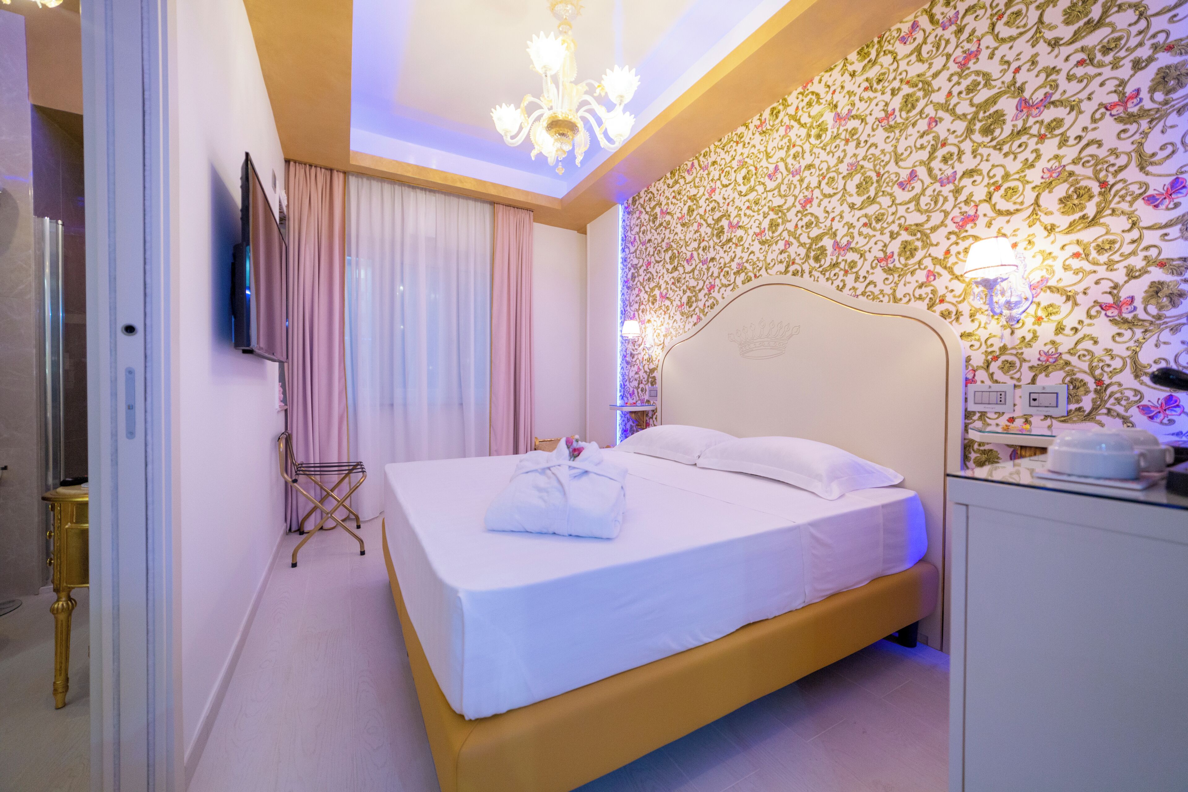 Camera d'albergo con un letto, una televisione, un lampadario e una parete decorata.