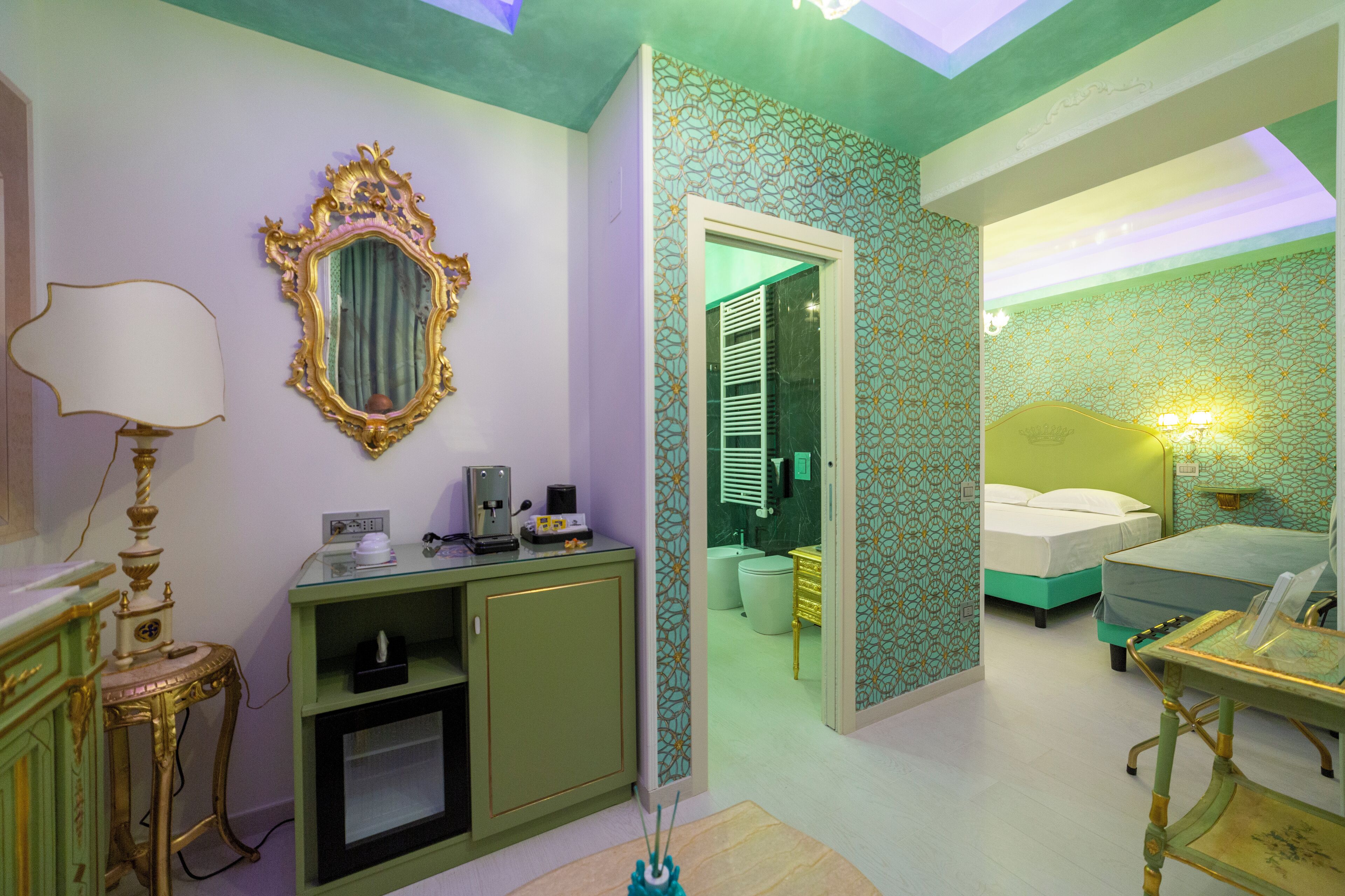 A room with a bed, a desk, a mirror, and a bathroom visible through an open door.
