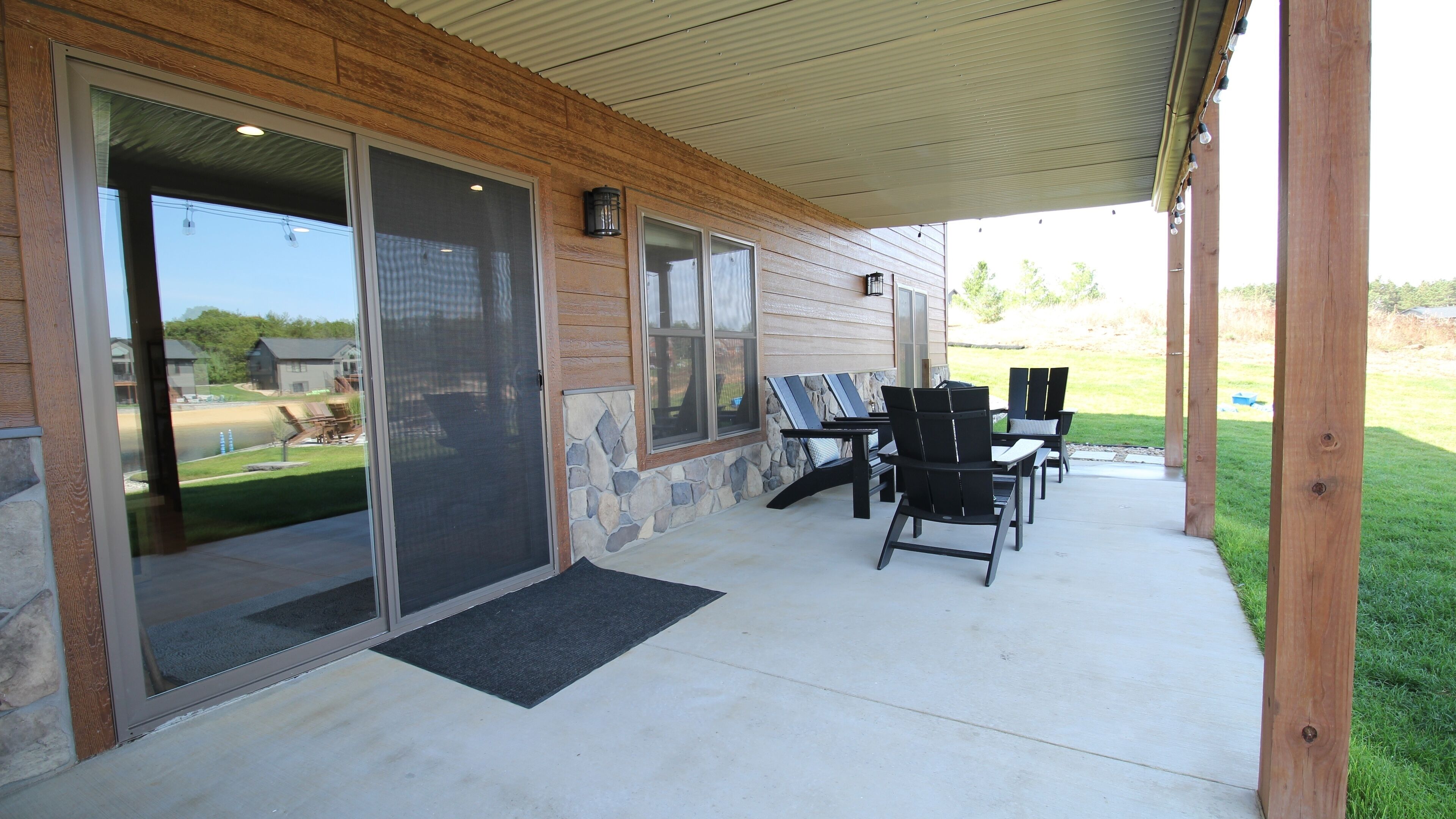 Un patio couvert avec une façade en pierre et en bois, des portes-fenêtres coulissantes et du mobilier d’extérieur.