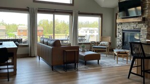 A spacious living room with a high ceiling, a stone fireplace, and large windows offering a view of the outside. - Kokomo Cabin: Cozy Fires, Family Fun & Lake Views (Germantown)