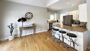 Una cucina moderna con pavimento in legno, mobili bianchi, un frigorifero in acciaio inossidabile e un angolo bar con sgabelli.