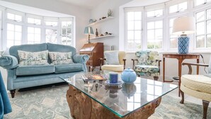 Un salon avec un canapé bleu, une table basse en verre et une table d’appoint en bois.