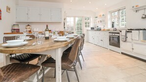 Une cuisine spacieuse avec des meubles blancs, une table à manger pour six personnes et une grande fenêtre qui laisse entrer la lumière naturelle.