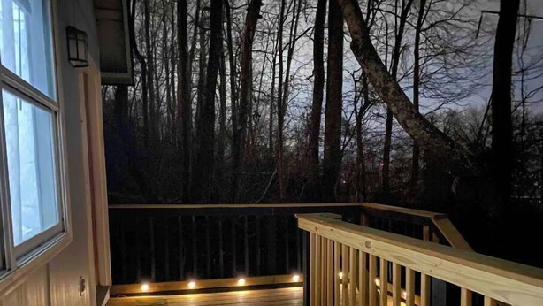 Una terraza de madera con barandillas, rodeada de árboles e iluminada con luces colgantes.