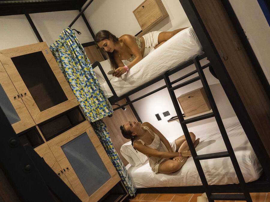 Una cama litera con dos niveles, cada uno con una almohada y un pequeño mueble de madera.