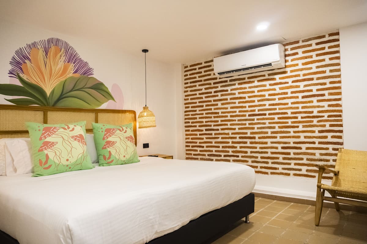 A hotel room with a brick-patterned wall, a bed with green and white bedding, and a wicker chair.