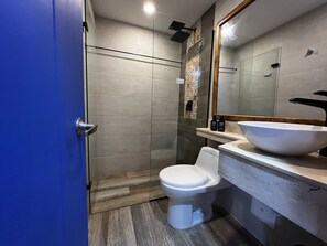 A modern bathroom with a glass shower enclosure, a white toilet, and a large mirror above a white sink with a vessel basin. - Los Patios Hostel (Cartagena)