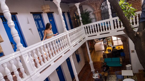 Un patio tradicional con baranda blanca, puertas azules y un área de descanso con mesas y sillas.