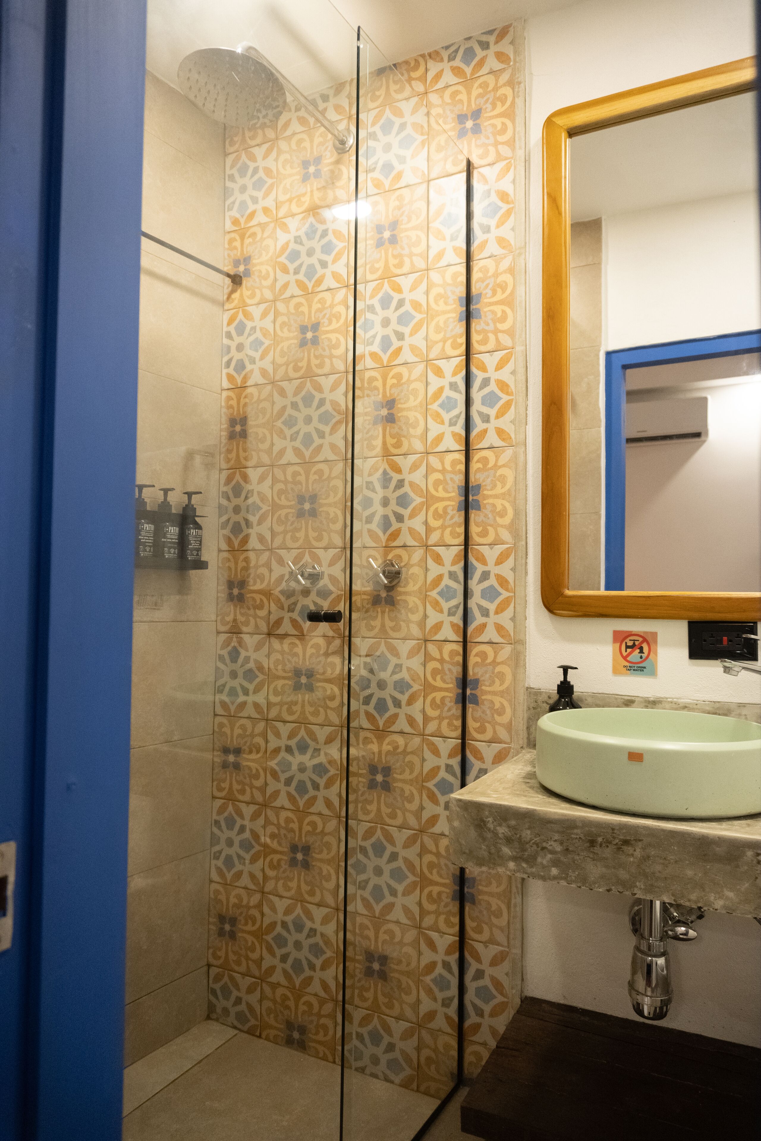 Et badeværelse med mønstret flisegulv, en bruser, en vask med spejl og toiletartikler på væggen.