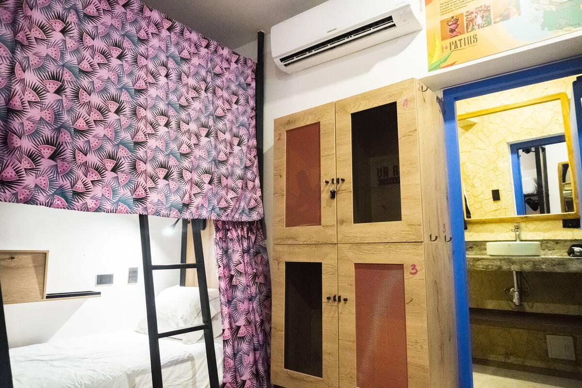 A room with bunk beds, a wooden wardrobe with numbered compartments, and a bathroom with a yellow mirror and sink.