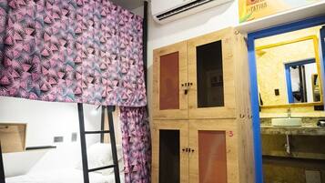 A room with bunk beds, a wooden wardrobe with numbered compartments, and a bathroom with a yellow mirror and sink.