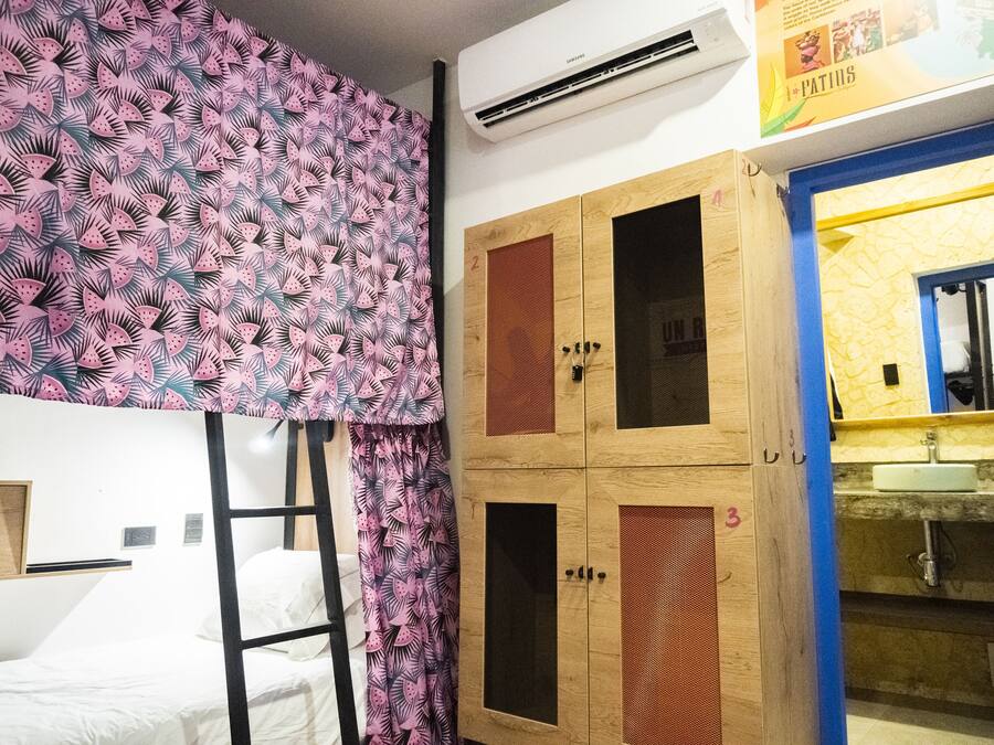 A room with bunk beds, a wooden wardrobe with numbered compartments, and a bathroom with a yellow mirror and sink.