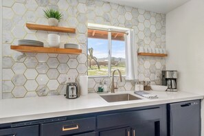 Una cocina con salpicadero de mármol blanco, estanterías de madera, una ventana con vistas y electrodomésticos modernos.