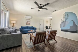 A living room with a ceiling fan, a blue sofa, a wooden coffee table, and a painting on the wall.