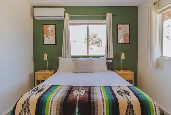 Un dormitorio con cama, dos mesitas de noche, una ventana con cortinas y un cuadro en la pared.