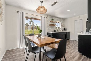Una cocina moderna con comedor, que incluye una mesa de madera, sillas negras y una lámpara colgante.