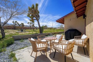 An outdoor patio with wicker furniture, a barbecue grill, and a view of the surrounding landscape.