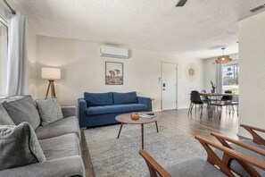 A modern living room with a blue sofa, a round coffee table, and a dining area with a table and chairs.