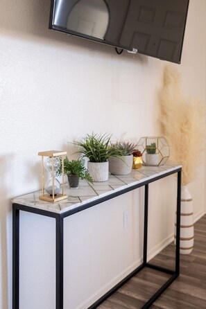 Una consola blanca con marco negro, decorada con plantas en macetas y una esfera de cristal.