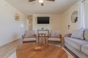 Una sala de estar con una mesa de centro de madera, dos sillones, un sofá, un televisor de pantalla plana montado en la pared y un ventilador de techo.