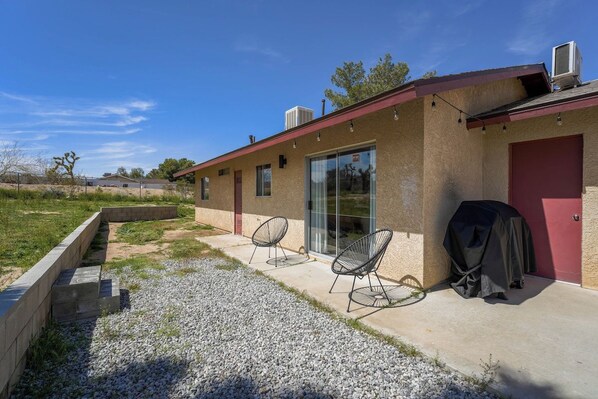 A modern building with a covered patio area, outdoor seating, and a barbecue grill.