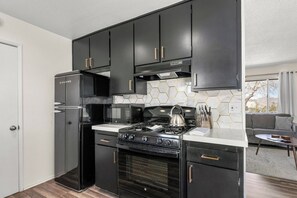A modern kitchen with black cabinets, a stainless steel refrigerator, a gas stove, and a microwave.