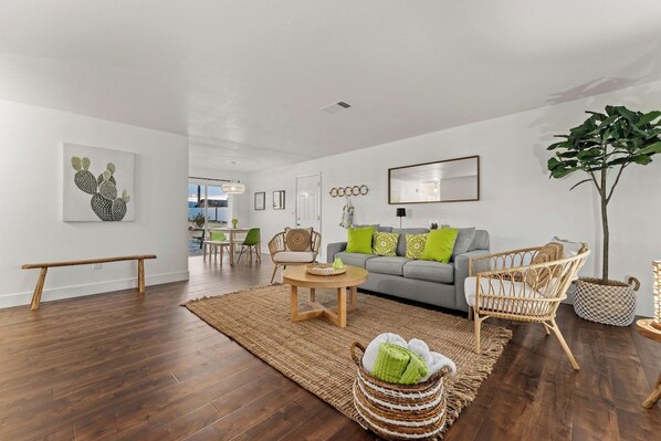 A modern living room with a grey sofa, wicker chairs, a coffee table, and a large plant.