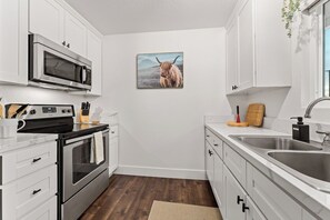 A kitchen with white cabinets, a microwave, an oven, a sink, and a painting of a yak on the wall.