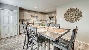 Una cocina moderna con armarios blancos, una mesa de comedor de madera y un elemento decorativo en la pared.