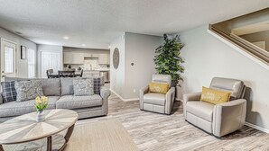 Una sala de estar moderna con un sofá gris, dos sillones, una mesa de centro y una planta grande.