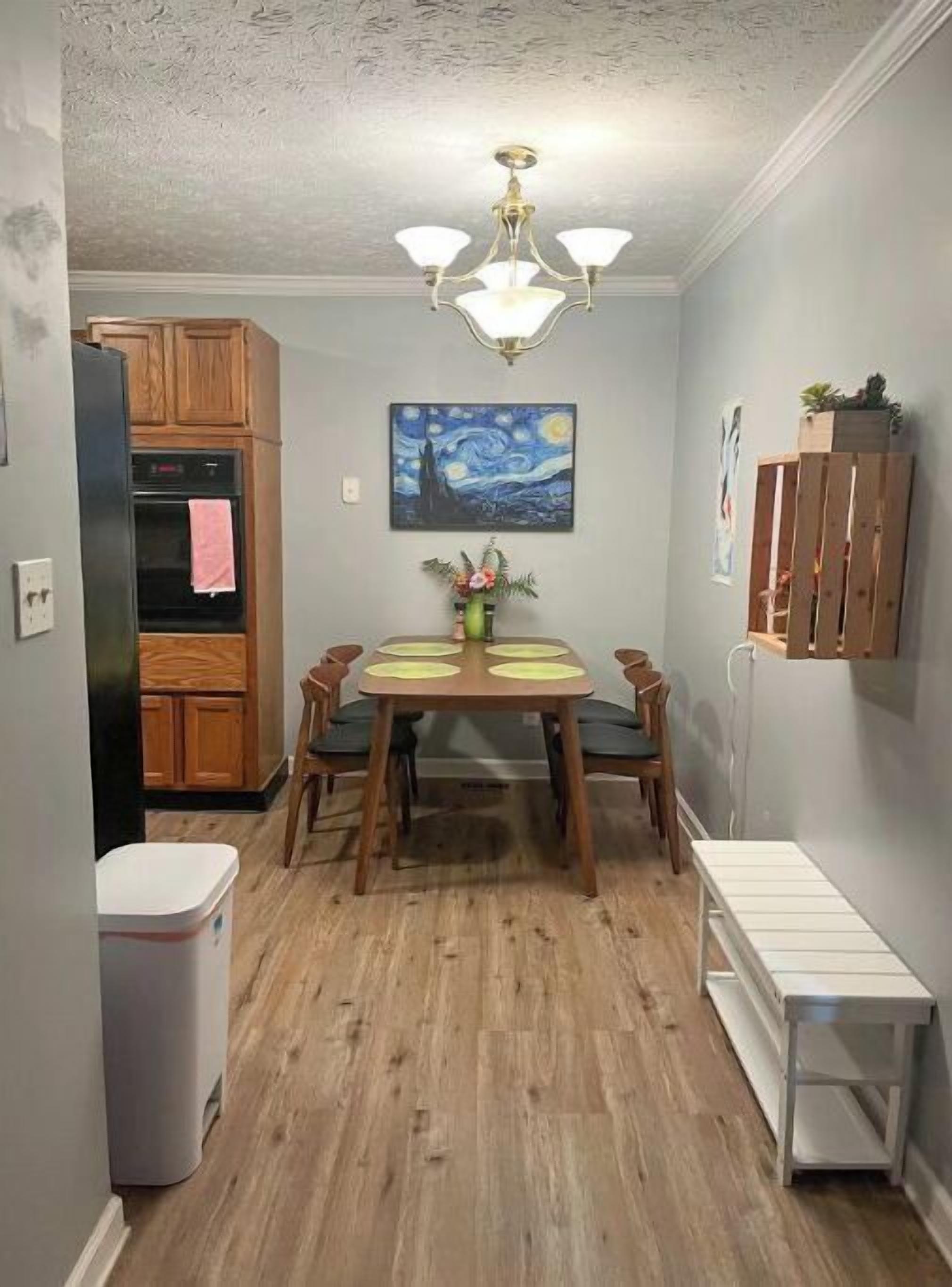 A dining area with a wooden table, chairs, a chandelier, and a painting on the wall.