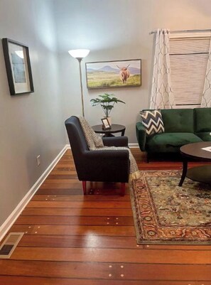 A living room with a dark leather armchair, a green sofa, a patterned rug, a framed picture of a cow, and a lamp. - Mountainside retreat 20 minutes from Downtown (Knoxville)