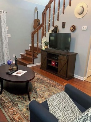 Uma sala de estar com escada de madeira escura, uma televisão sobre suporte de madeira, um globo e um tapete estampado.