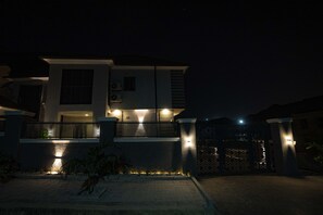 Une maison moderne à deux étages, dotée d’une entrée sécurisée par un portail, d’un éclairage extérieur et d’un jardin paysager à l’avant.