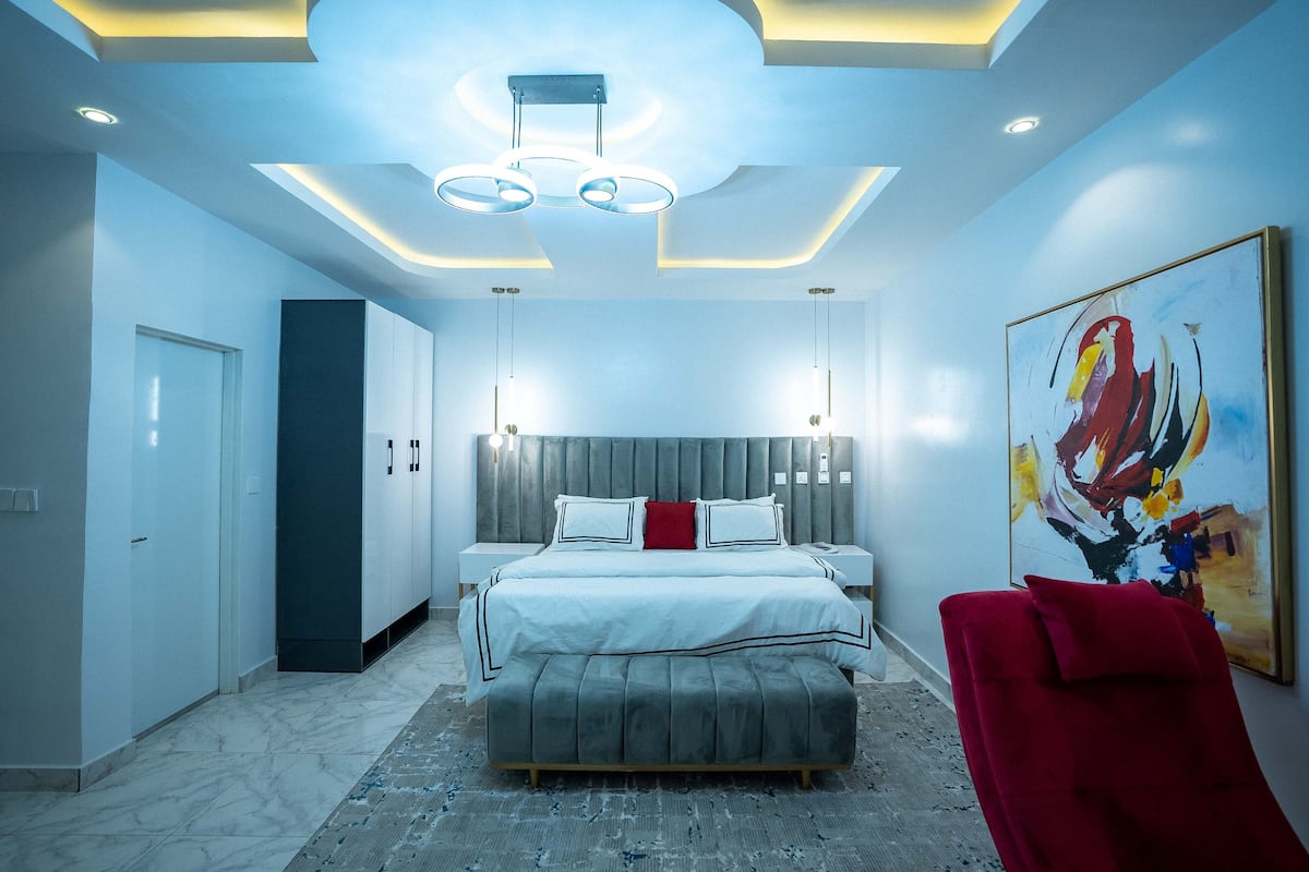 A modern bedroom with a large bed, bedside tables, a red chair, and a ceiling light fixture.