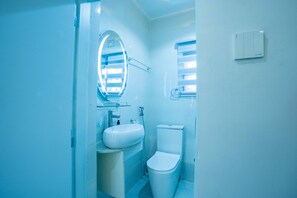 Une salle de bain avec un lavabo blanc, des toilettes, un miroir et un porte-serviettes.