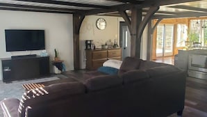 Una sala de estar con un sofá grande de color oscuro, un televisor de pantalla plana sobre un mueble bajo, una mesa de centro de madera y una mesita auxiliar con una planta.