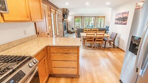 Een moderne keuken met houten kasten, een ingebouwd gasfornuis en een eethoek met houten stoelen en een tafel.