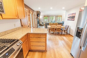 A modern kitchen with wooden cabinets, a built-in stove, and a dining area with a table and chairs.