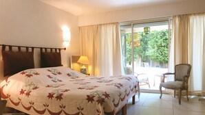 A hotel room with a large bed, a chair, a table, and a view of the outdoors. - Charming cocoon for 4p in nature, space, infinity pool (Châteauneuf-Grasse)