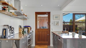 Eine moderne Küche mit Edelstahlgeräten, Holzregalen und einem großen Fenster mit Blick ins Freie.