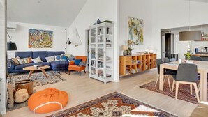 Ein geräumiges Wohnzimmer mit einem blauen Sofa, einem orangenen Sitzsack und einer weißen Regaleinheit, die mit Büchern und Dekoration gefüllt ist.
