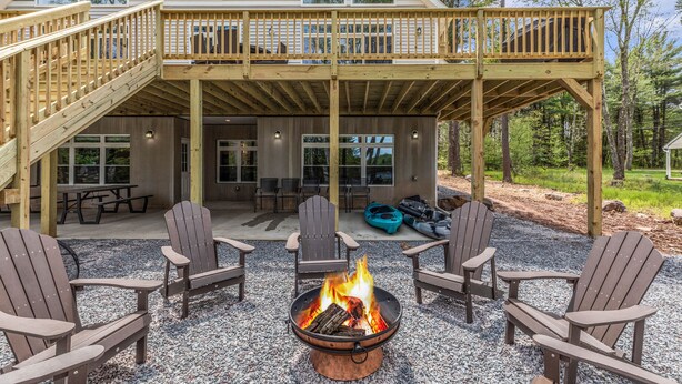 A covered outdoor deck with Adirondack chairs and a fire pit. - Luxurious Chalet in Blakeslee: Game Room, Hot Tub, Lake Access, Fire pit (Blakeslee)