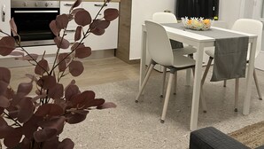 Una cocina moderna con armarios blancos, horno empotrado y comedor con mesa y sillas blancas.
