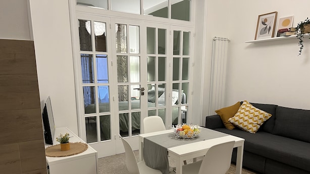 Una sala de estar moderna con comedor, un sofá gris y una mesa blanca con sillas.